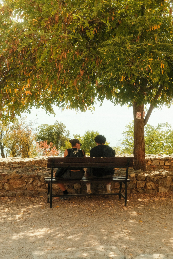 Two people sitting on a bench under a tree